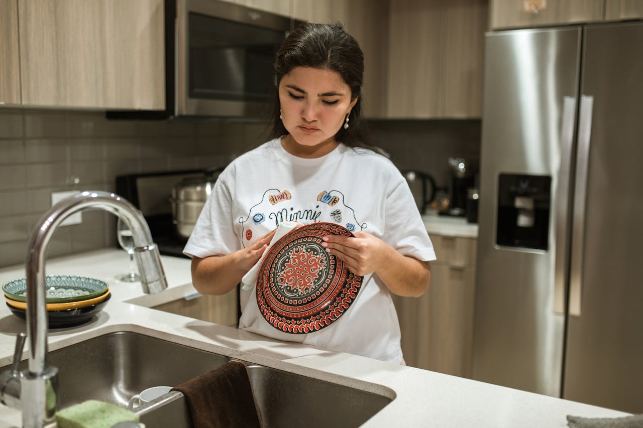 Young woman wiping a plate in a stylish kitchen setting, showcasing daily chores.
